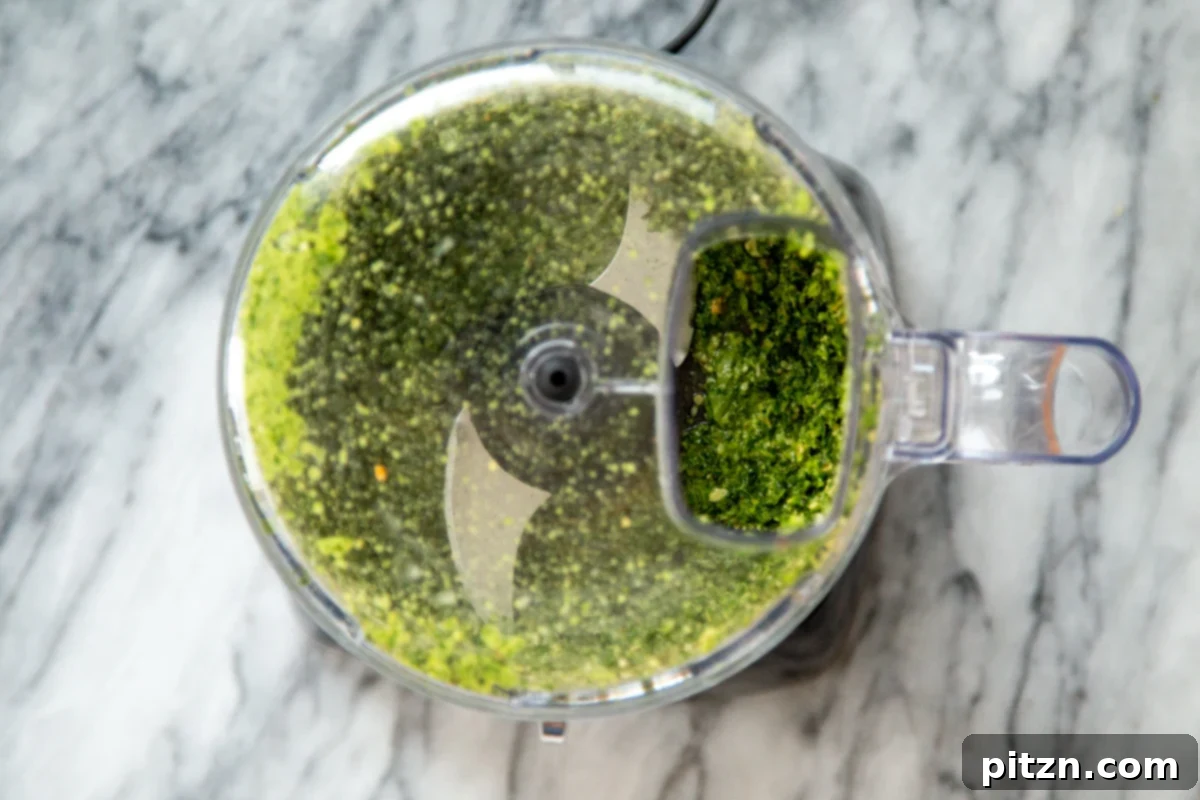 Freshly blended basil pesto inside a food processor, showcasing its rich green color and smooth texture.