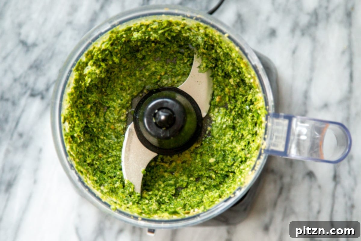 A close-up of vibrant green homemade basil pesto in a food processor, highlighting its fresh texture.