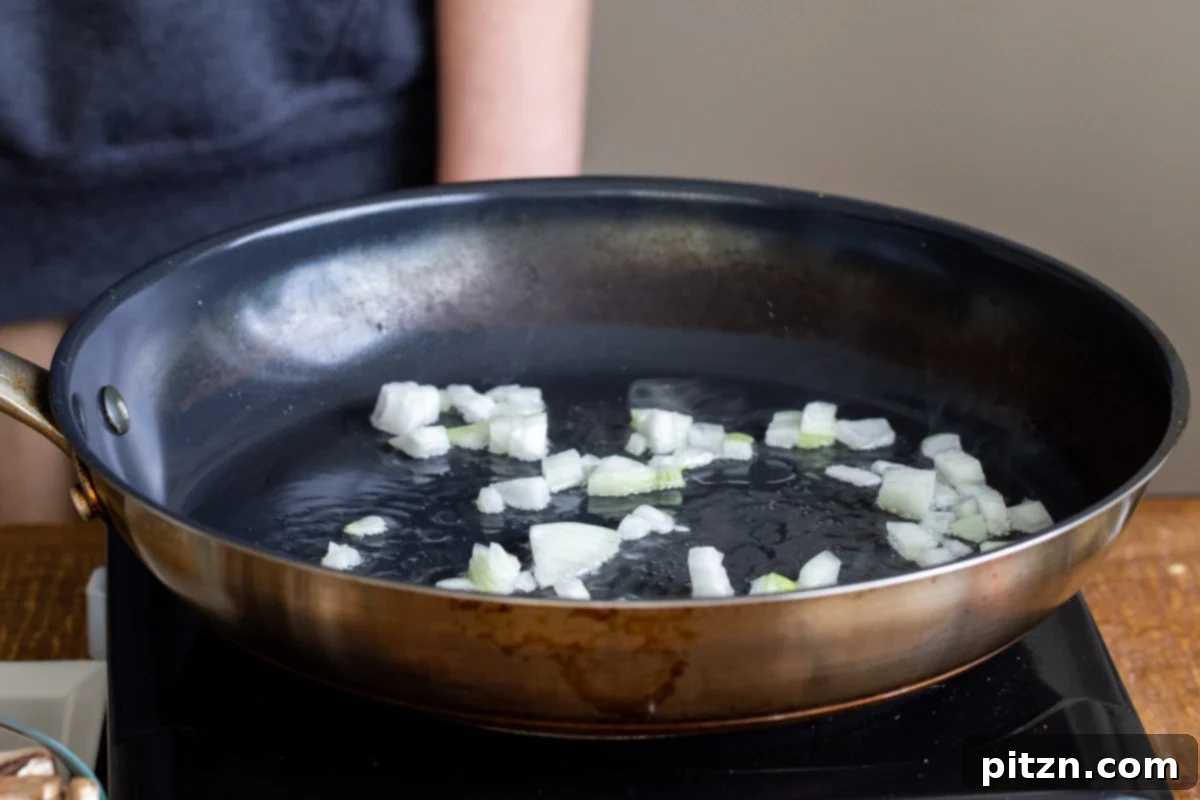 Minced onions being gently sautéed in a black skillet, forming the aromatic base for the lasagna.