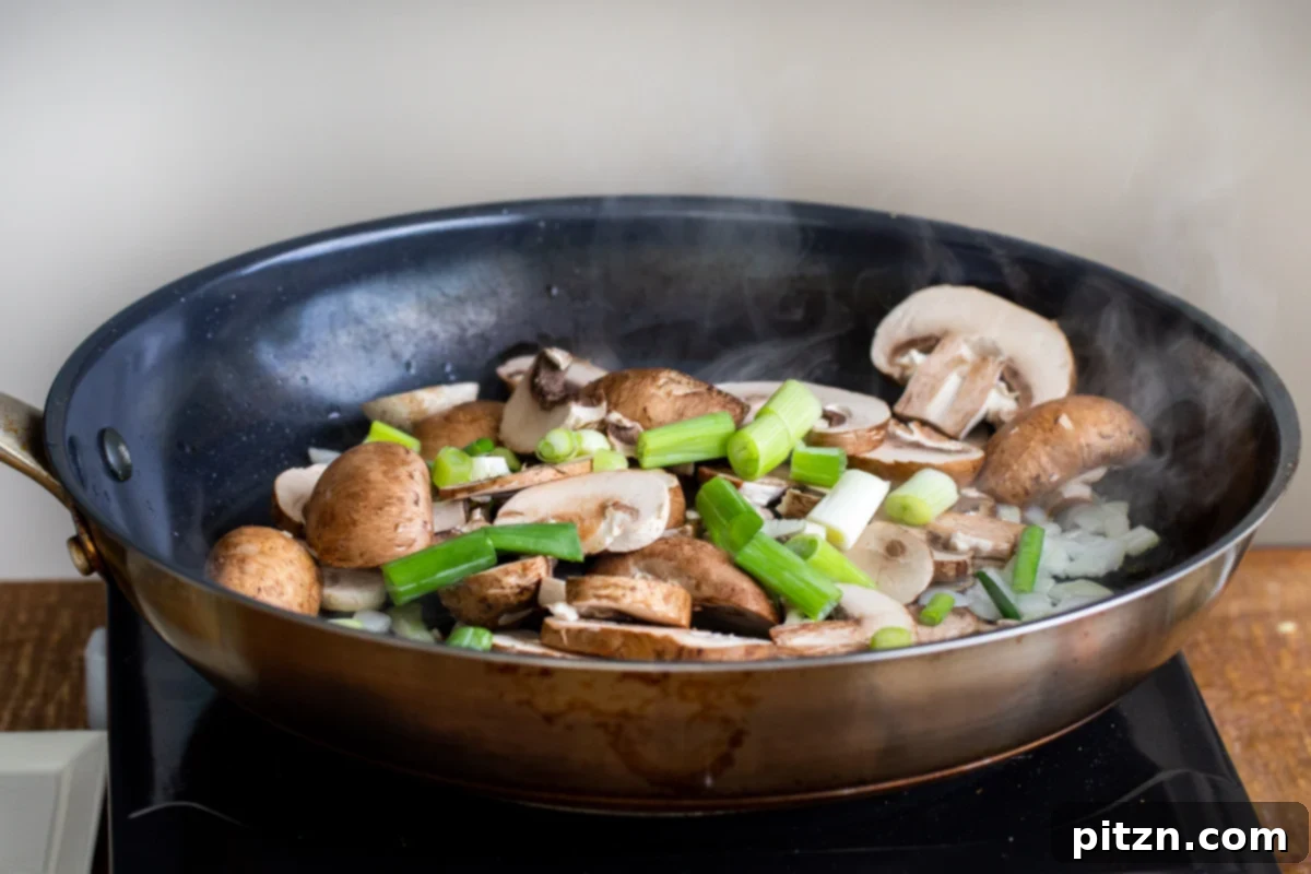 A colorful mix of onions, mushrooms, and green onions sautéing together in a black skillet, releasing their enticing aromas.