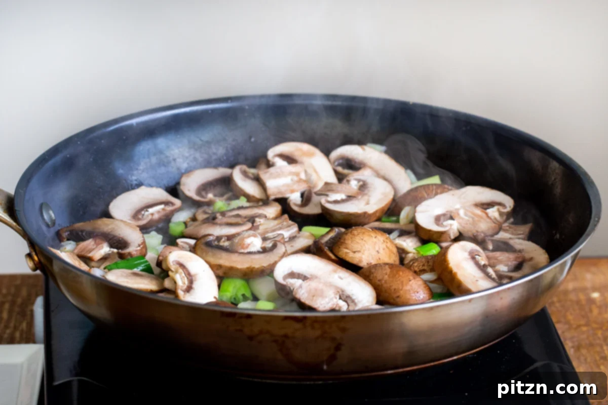Thinly sliced mushrooms and green onions sizzling in a black skillet, beginning to caramelize and brown.