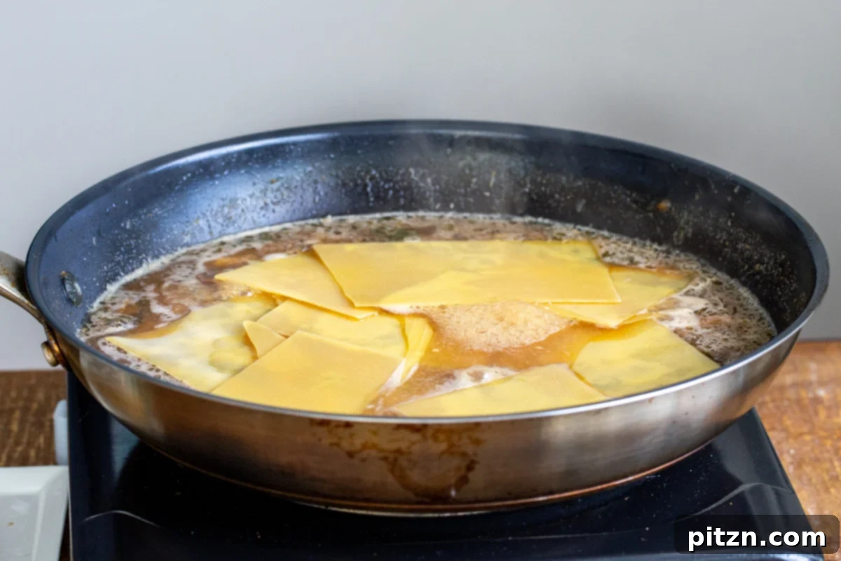 Broken lasagna noodles being carefully added to the simmering mushroom broth in a skillet, preparing for the stovetop lasagna.