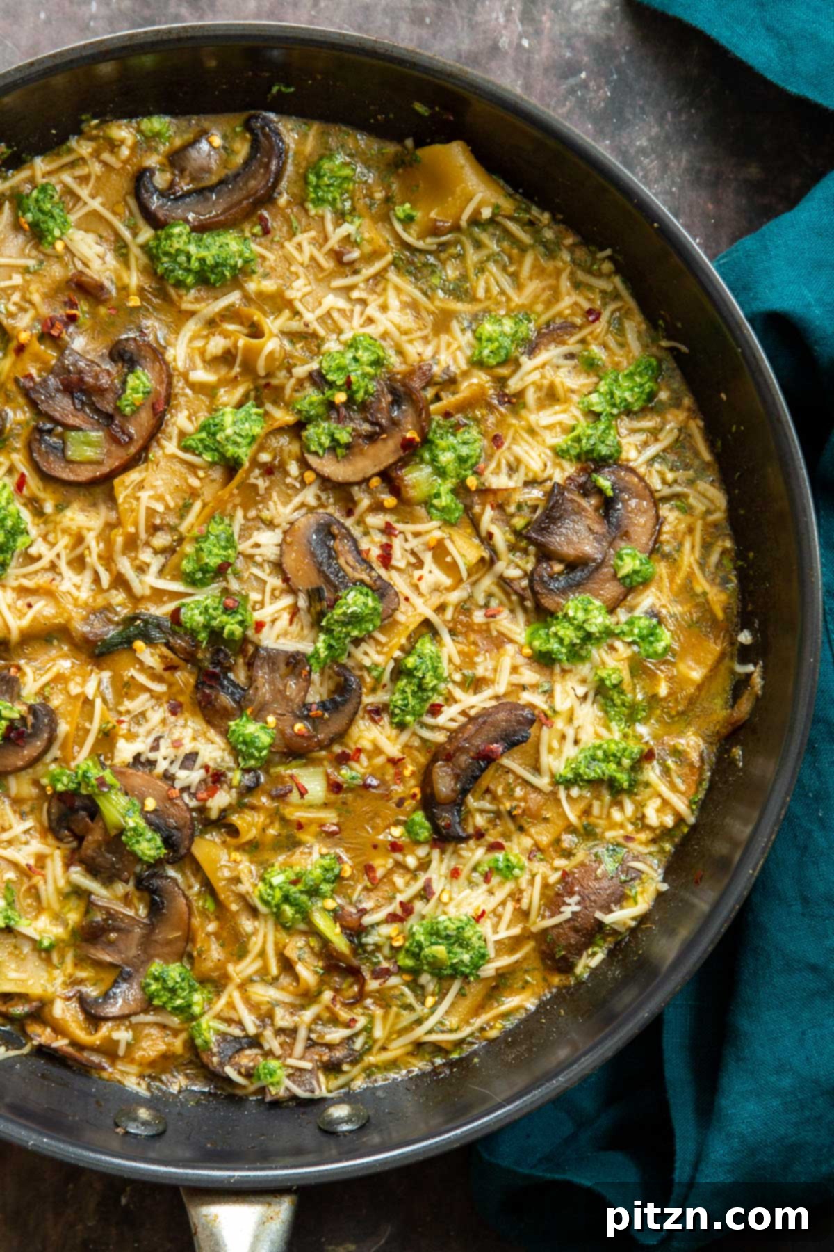 An overhead shot of a black skillet filled with hearty vegan one-pan mushroom and pesto lasagna, freshly cooked and steaming.