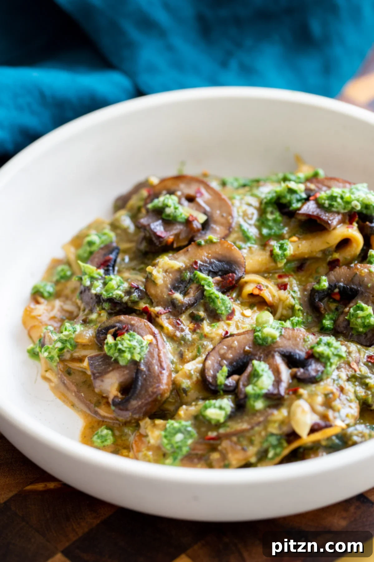 A close-up of vegan mushroom pesto skillet lasagna served in a white bowl, garnished with fresh basil pesto dollops.