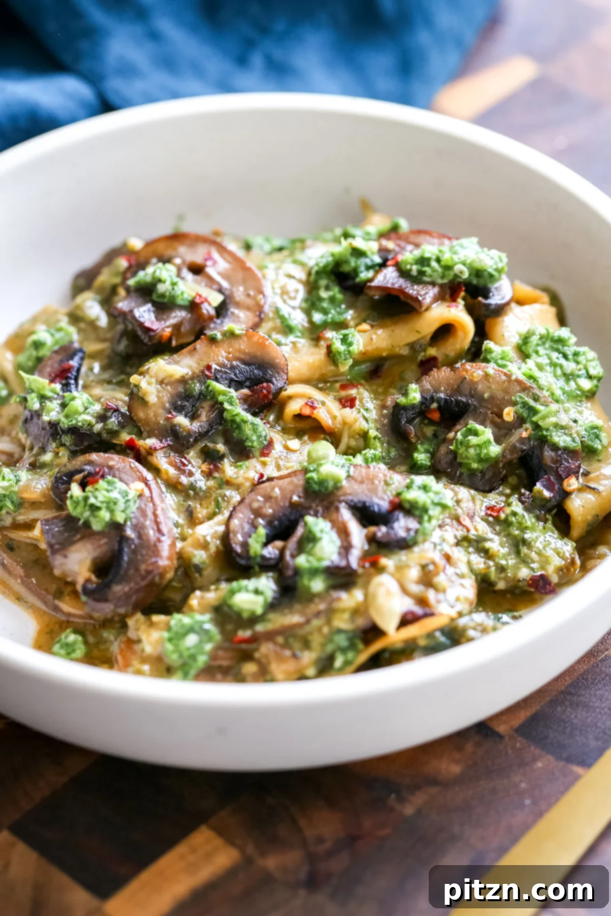 A generous serving of vegan skillet pesto lasagna in a bowl, showcasing the rich sauce, tender noodles, and mushroom toppings.