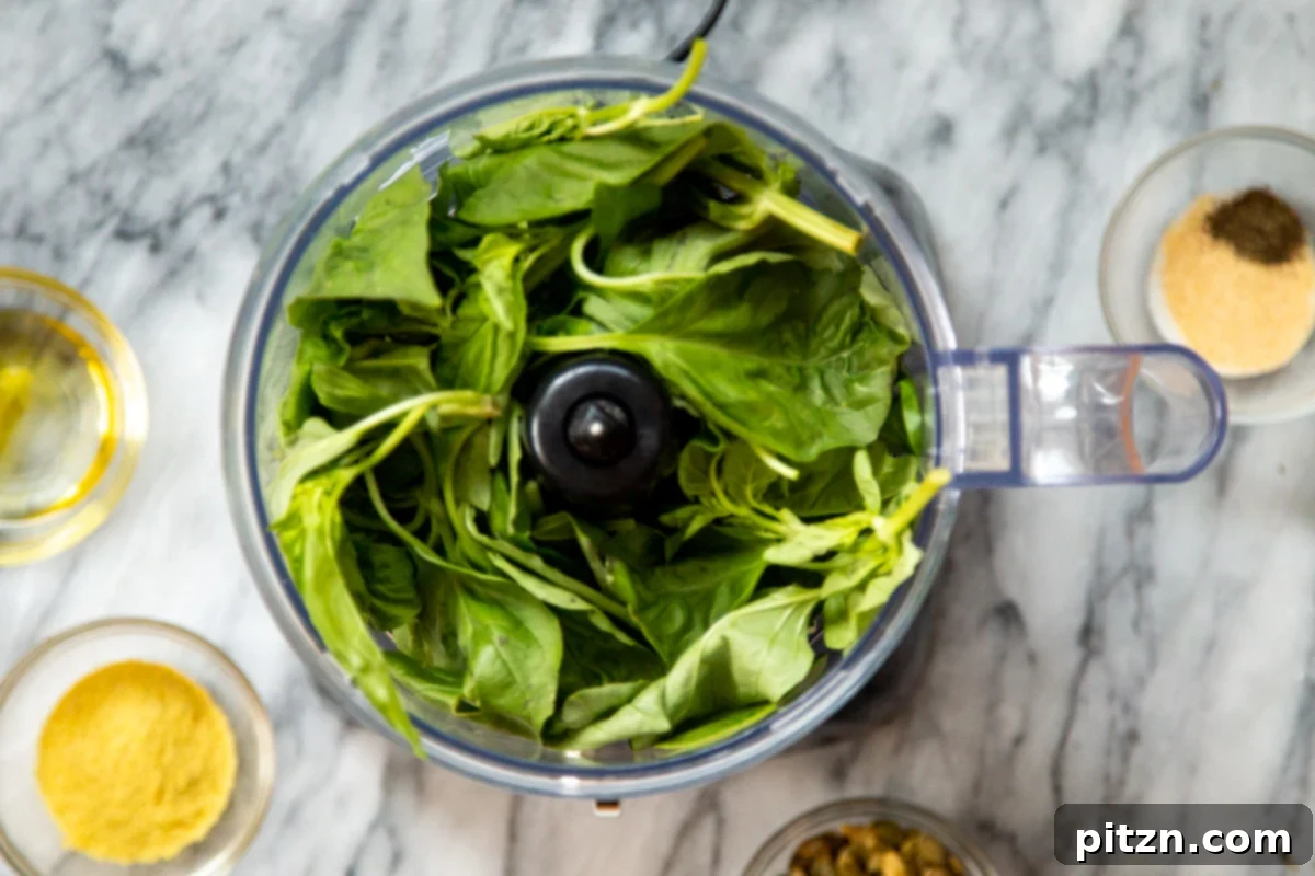 Fresh basil leaves being added into a food processor, ready for pesto making.