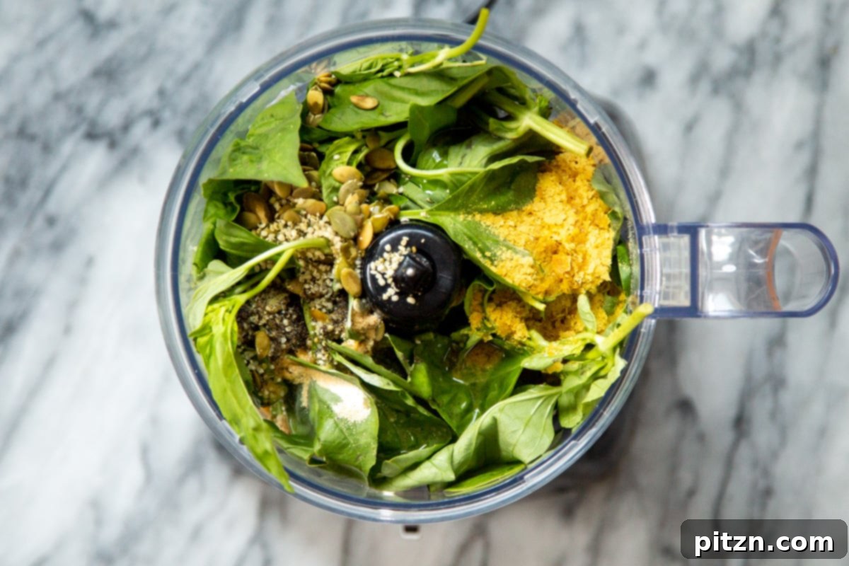 Pumpkin seeds and nutritional yeast being poured into a food processor, adding to the pesto ingredients.
