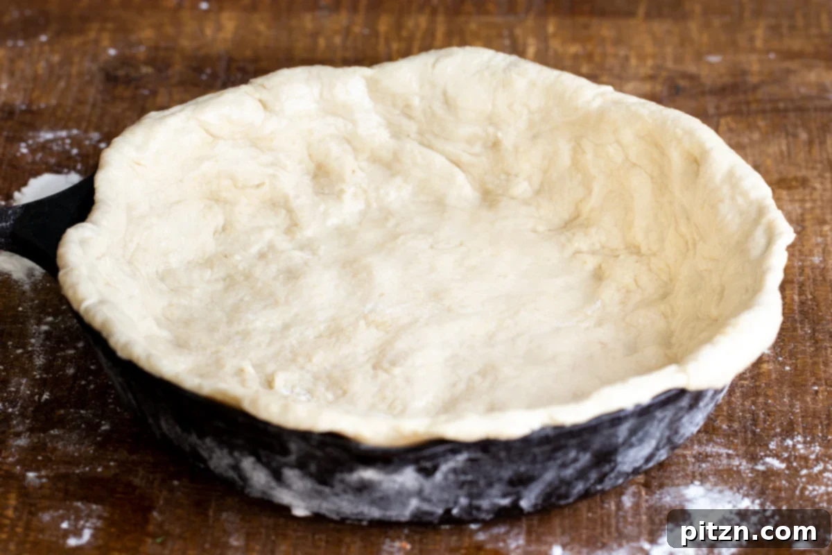 Deep Dish Pizza with a Pretzel Twist 12 A black cast iron skillet being skillfully lined with the pretzel pizza crust dough, pressed firmly into the bottom and up the sides to form a deep dish shape.