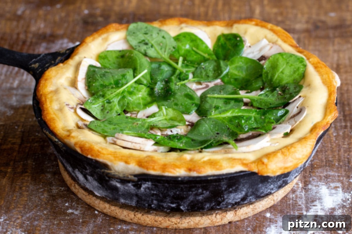 Deep Dish Pizza with a Pretzel Twist 16 A vibrant vegan pretzel crust pizza in a black skillet, fully assembled with mushrooms and fresh spinach over cheese, ready for its final bake.