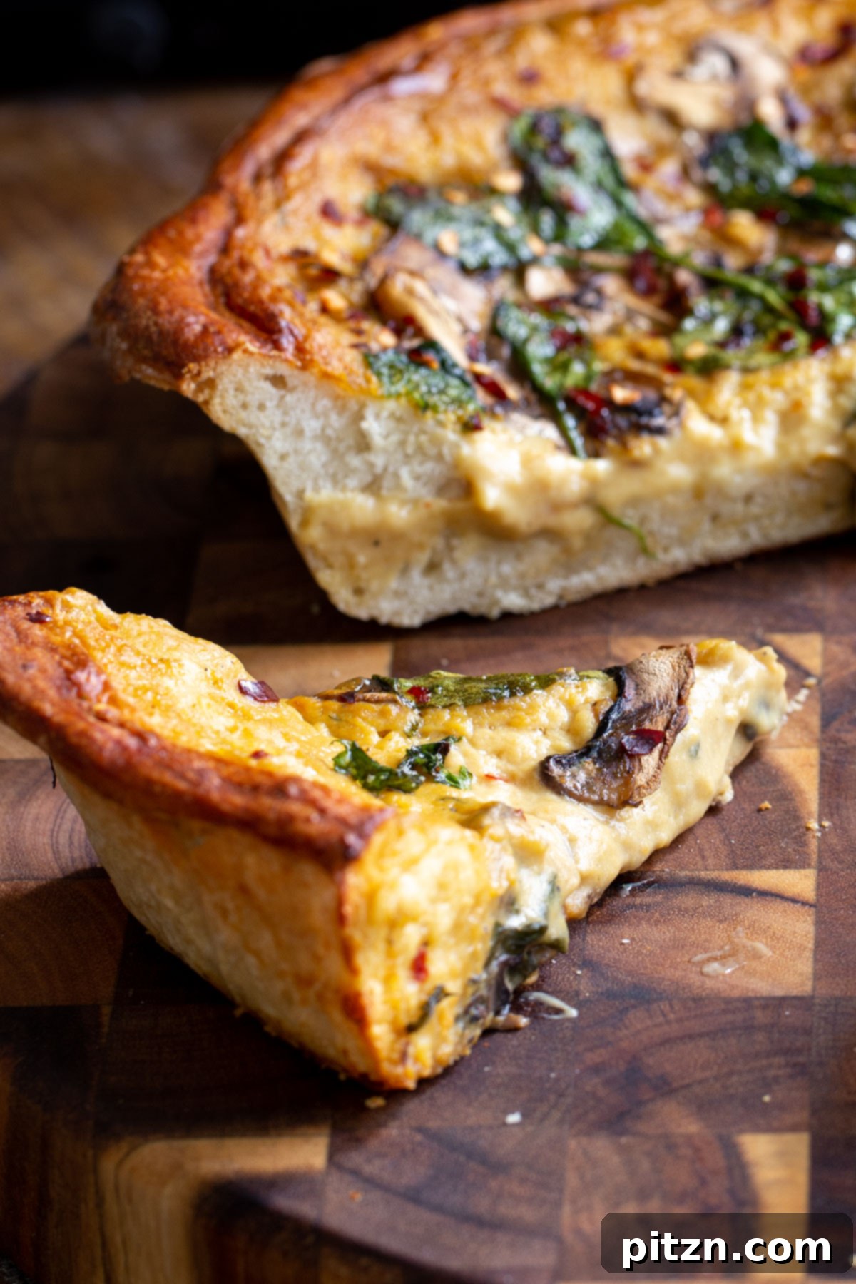 Deep Dish Pizza with a Pretzel Twist 17 A large, inviting slice of vegan deep dish pretzel crust pizza, showcasing its thick layers of cheese, mushrooms, and spinach, presented on a wooden board.