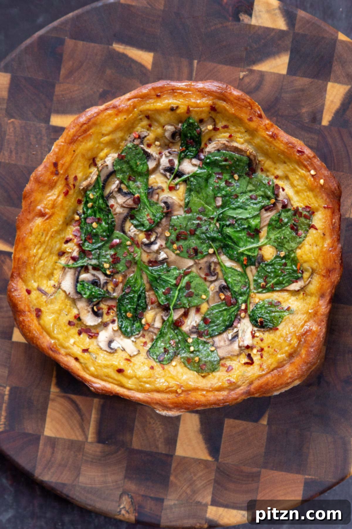 Deep Dish Pizza with a Pretzel Twist 18 A freshly baked vegan pretzel crust pizza, garnished with cheese sauce, spinach, mushrooms, and a sprinkle of pepper flakes, cooling on a wooden board.