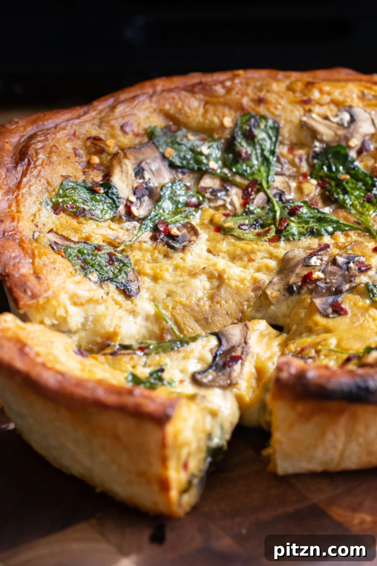 Deep Dish Pizza with a Pretzel Twist 5 A generously filled vegan deep dish pretzel crust pizza, overflowing with creamy cheese sauce, earthy mushrooms, and tender spinach, in a dark pan on a wooden surface.