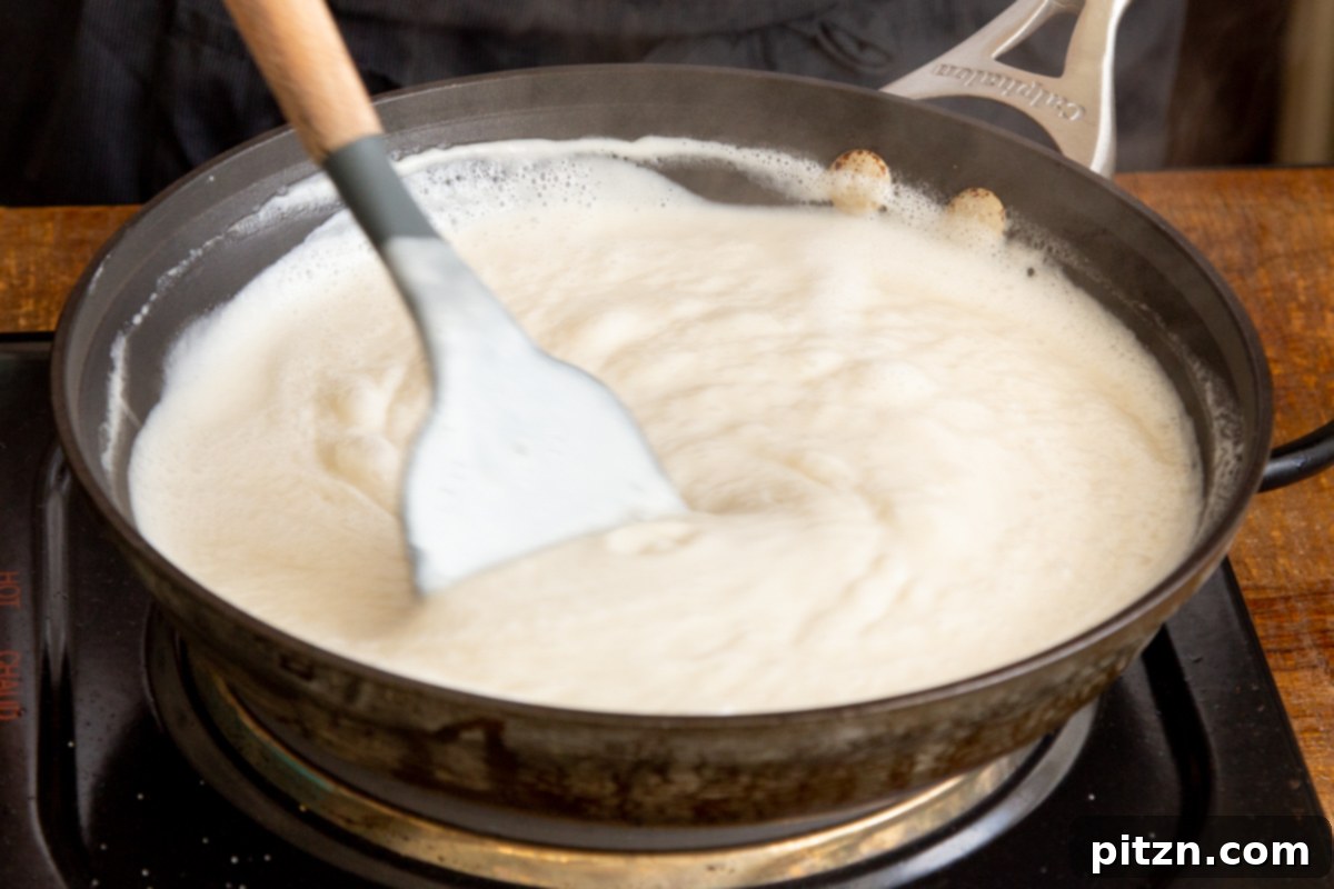Plant-Based Tiramisu Tray Bake 18 A close-up of vegan cashew mascarpone cream being reduced and stirred in a saucepan, highlighting its smooth, rich texture as it thickens.