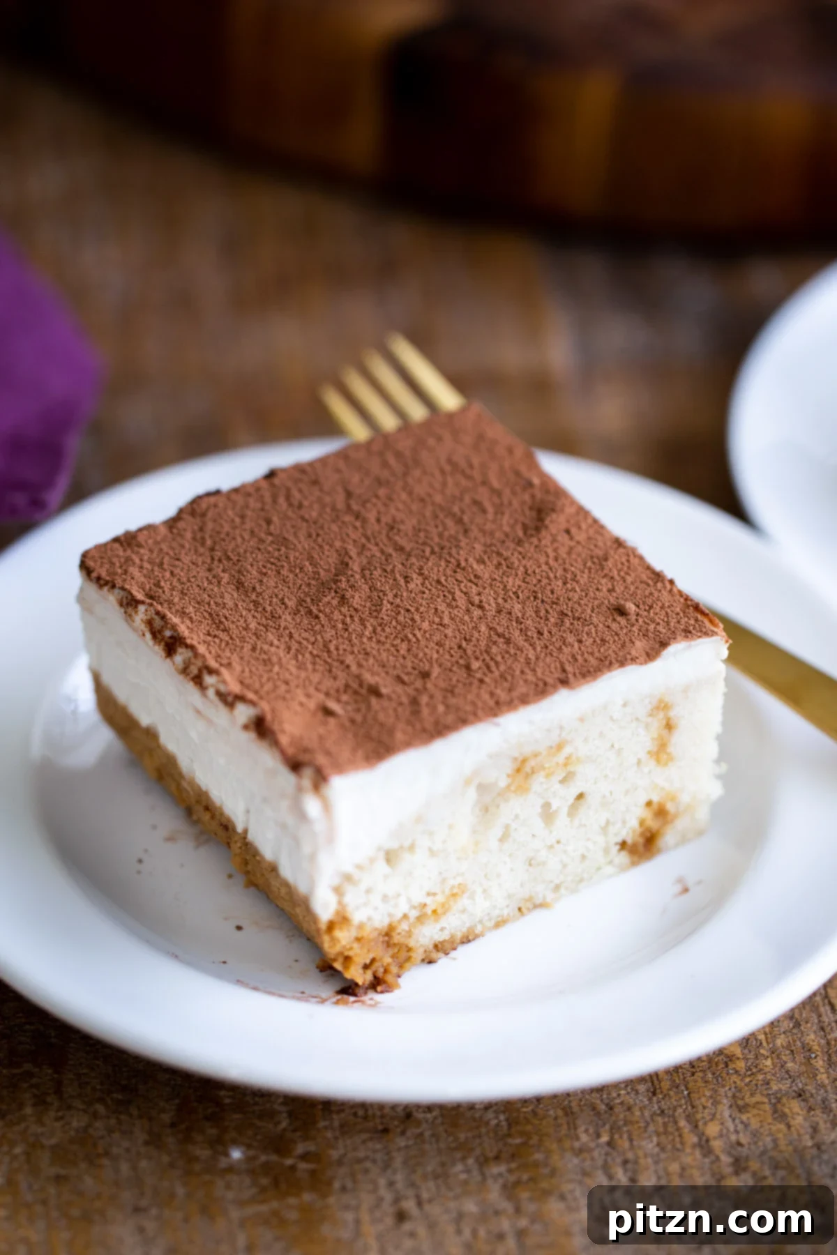 Plant-Based Tiramisu Tray Bake 20 A luxurious slice of vegan tiramisu cake, featuring a mascarpone topping dusted with cocoa, elegantly presented on a white plate, inviting a delicious tasting.