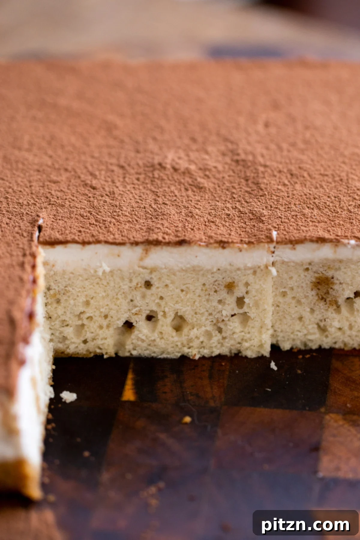 Plant-Based Tiramisu Tray Bake 4 An entire vegan tiramisu sheet cake, beautifully dusted with cocoa powder, resting on a rustic wooden board, ready to be sliced and served.