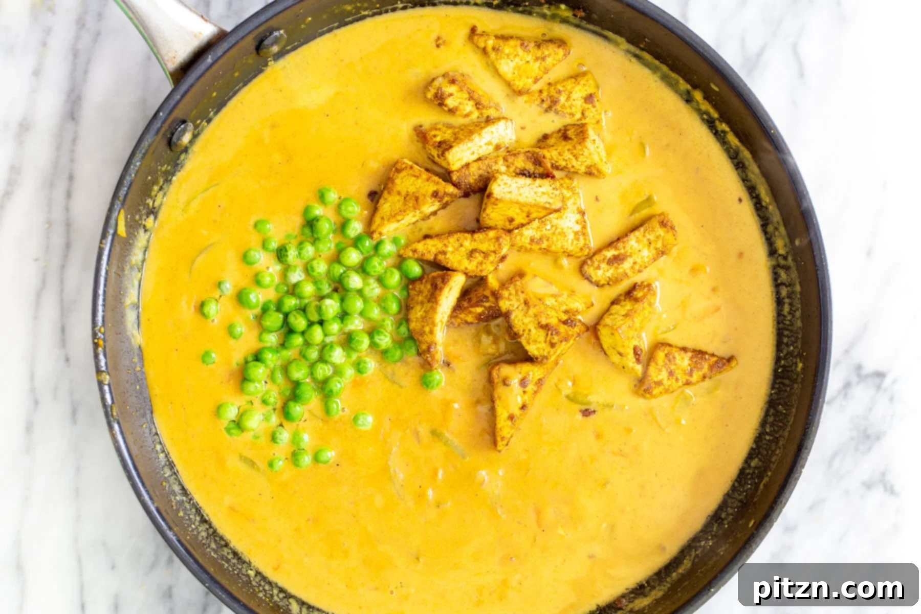 Vibrant Malaysian Tofu Curry 14 Crispy tofu and peas being added to a sautéing pan with coconut curry