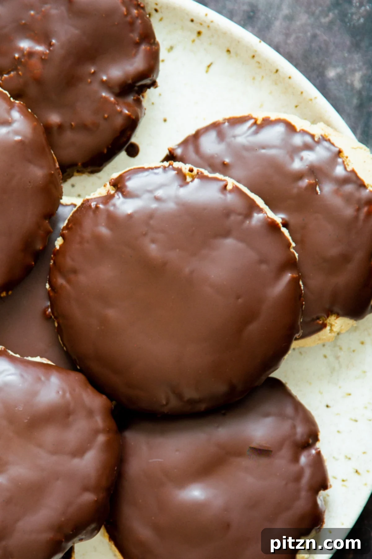 The Ultimate Vegan Gluten-Free Snickers Cookies 2 A white plate showcasing several delectable Vegan Snickers Cookies, each generously coated with a luscious chocolate glaze, highlighting their soft texture and appealing presentation.