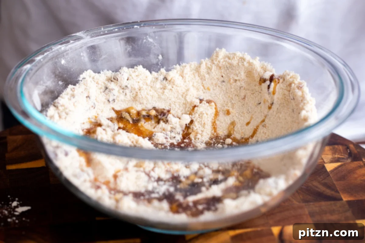 The Ultimate Vegan Gluten-Free Snickers Cookies 11 Maple syrup being poured into the glass bowl with dry ingredients, dates, and nuts, initiating the dough-making process.