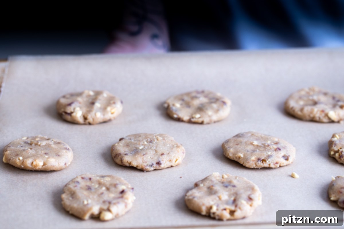 The Ultimate Vegan Gluten-Free Snickers Cookies 13 Unbaked vegan Snickers cookies, shaped into flat disks, neatly arranged on a parchment-lined cookie sheet, ready for the oven.