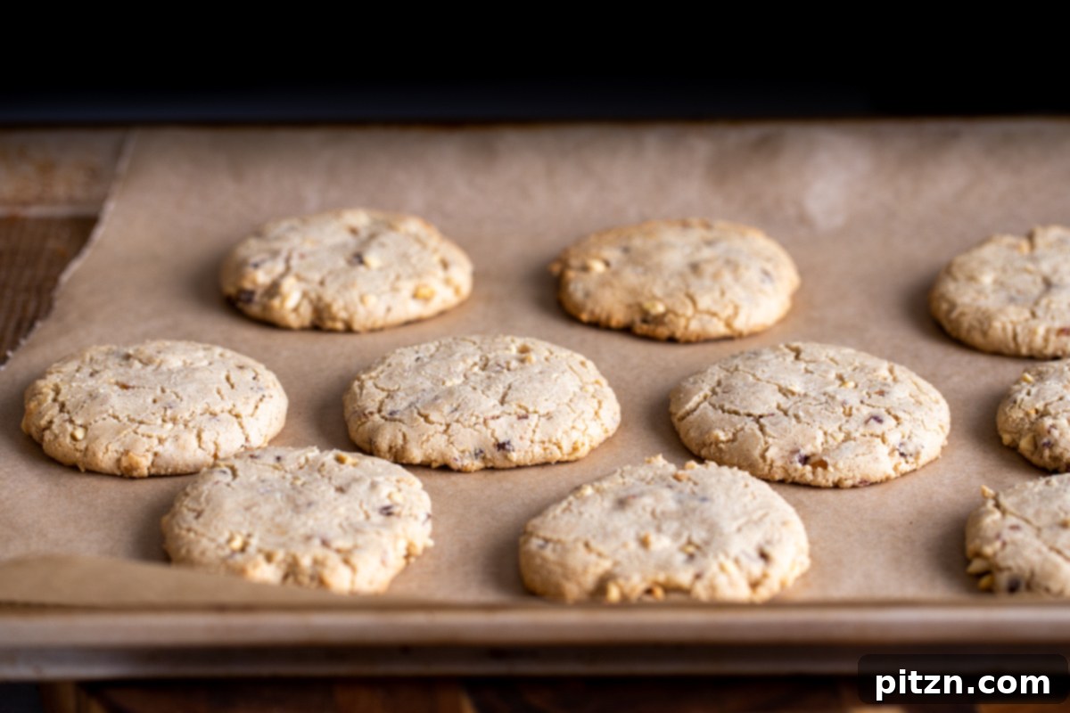The Ultimate Vegan Gluten-Free Snickers Cookies 14 Freshly baked vegan Snickers cookies, with golden-brown edges, cooling on a cookie tray after being removed from the oven.