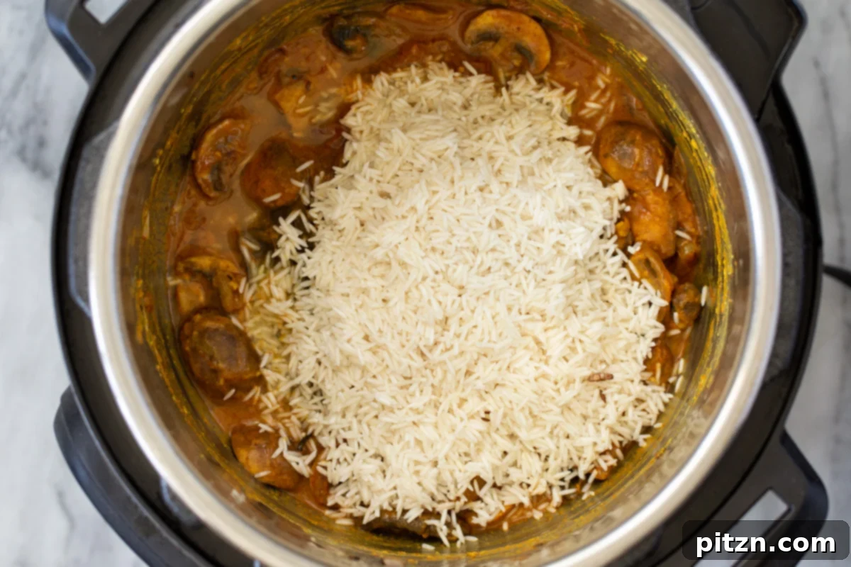 Fragrant Mushroom Biryani 17 Fluffy, drained rice being carefully added in a layer over spicy mushrooms in an Instant Pot, prepared for the next cooking phase.