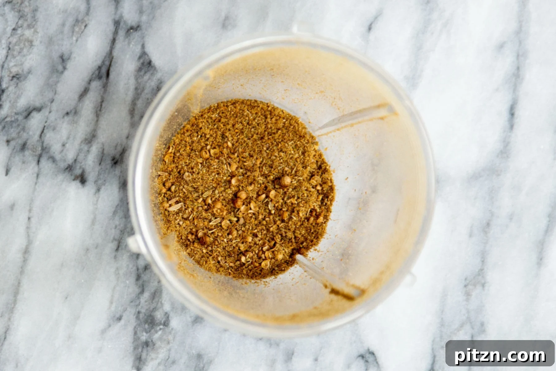Ground coriander and fennel seeds in a spice grinder, showcasing their coarsely textured form.