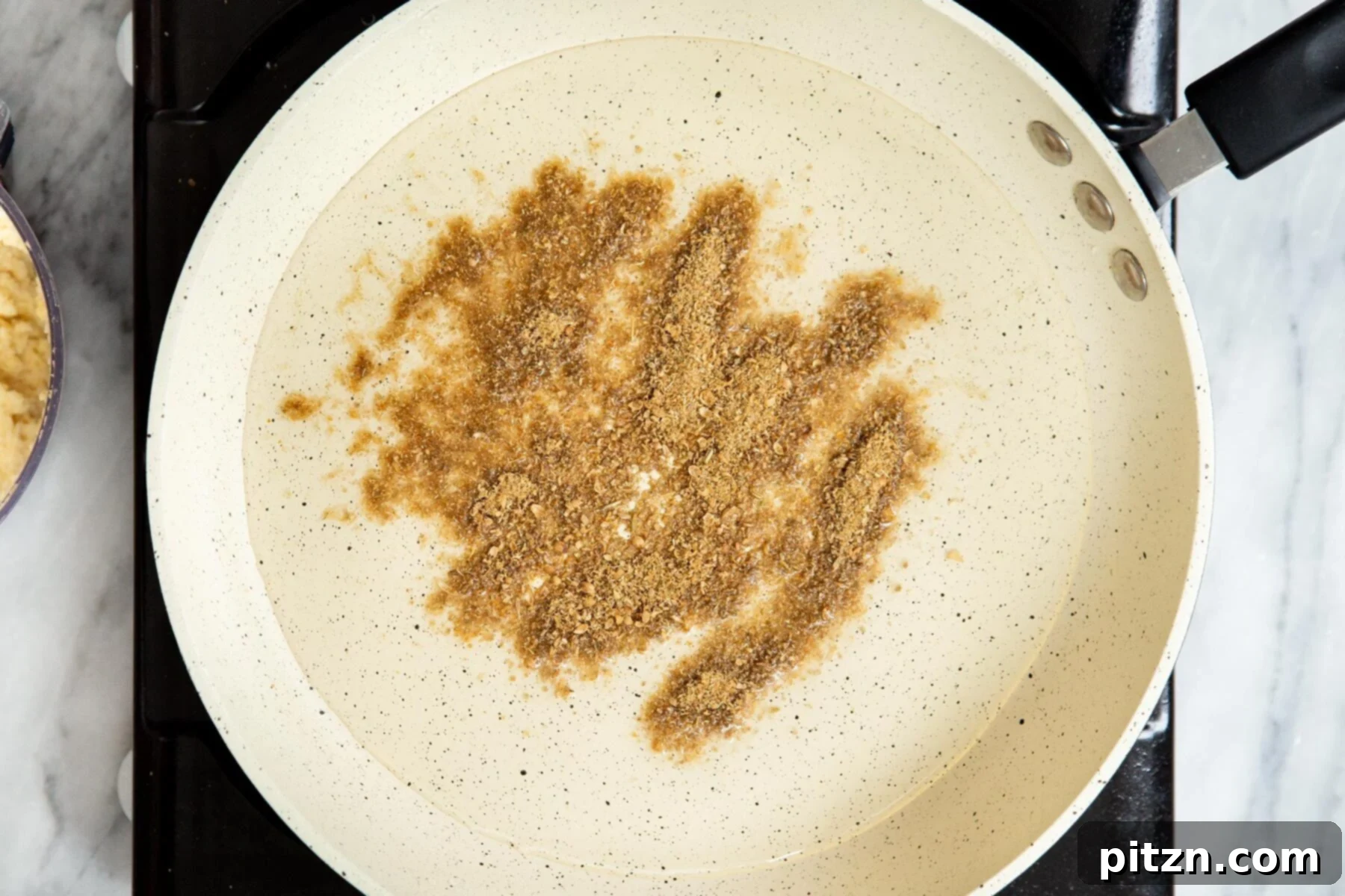 Ground spices, including fennel and coriander, gently frying in oil in a saucepan, releasing their aromatic fragrance.