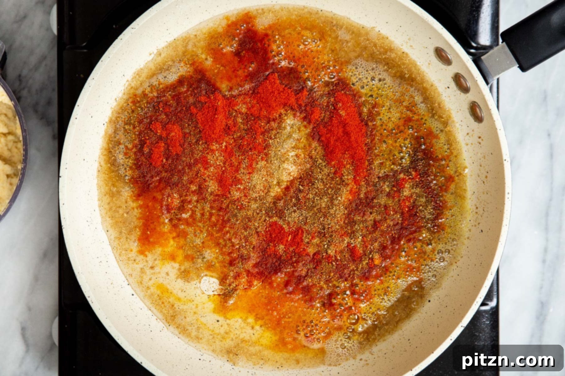 More ground spices being added to the frying mixture in a sauté pan, intensifying the aroma.