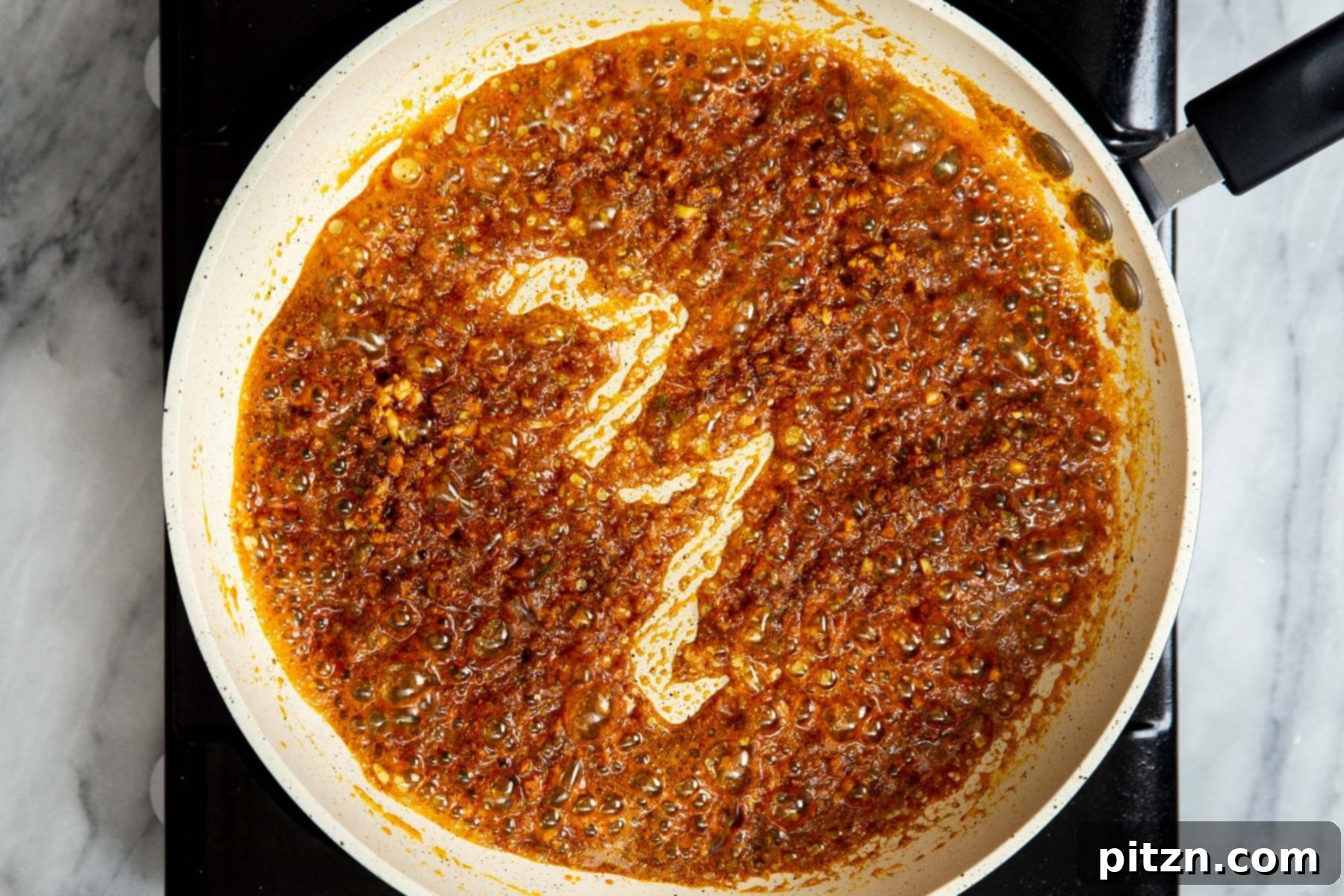 The Indian spice paste, rich with ginger, garlic, and chilies, actively frying in a sauté pan, developing deep flavors.