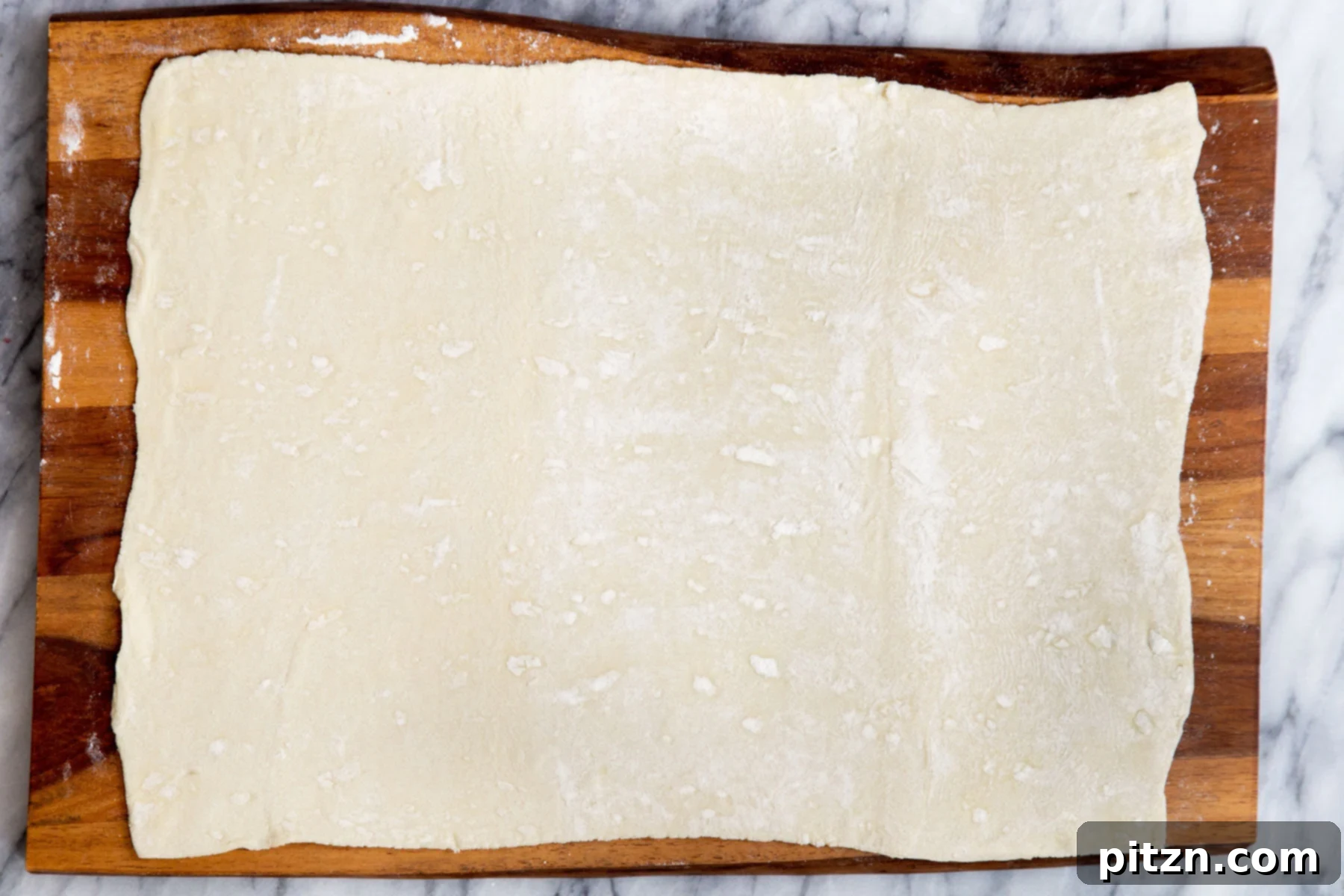 A sheet of puff pastry being carefully rolled out on a chopping board, preparing it for the filling.