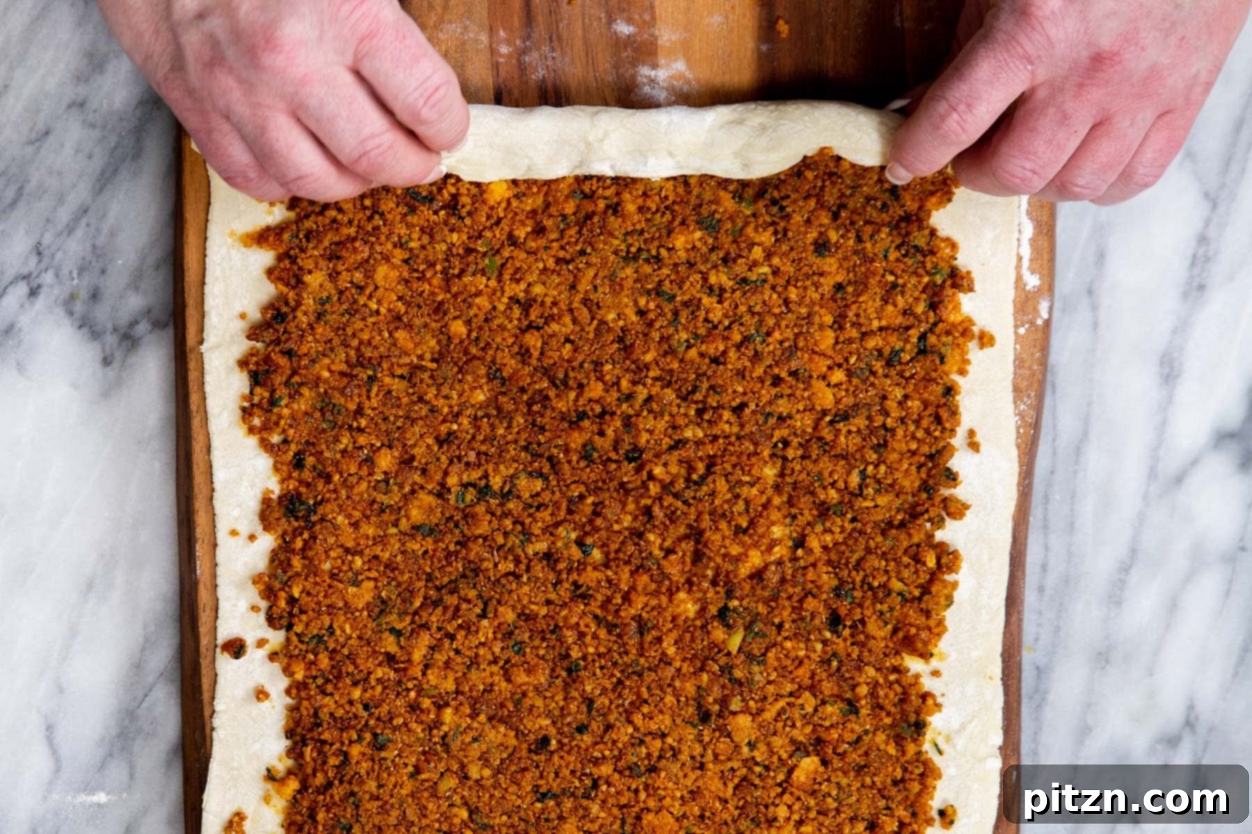 A sheet of puff pastry with lentil filling in the process of being rolled up from the long side to create pinwheels.