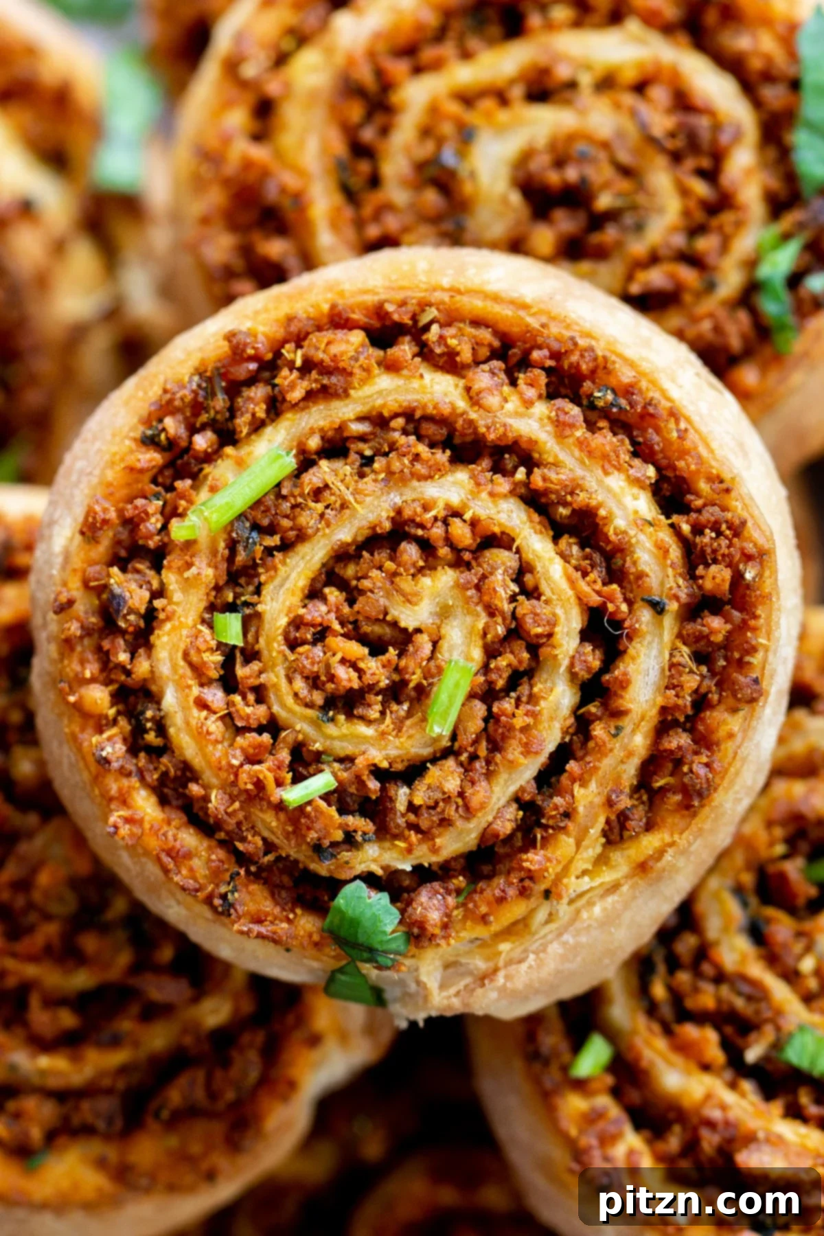 Close-up view of a platter showcasing perfectly baked puff pastry pinwheels, revealing layers of flaky pastry and a rich, spiced lentil filling.