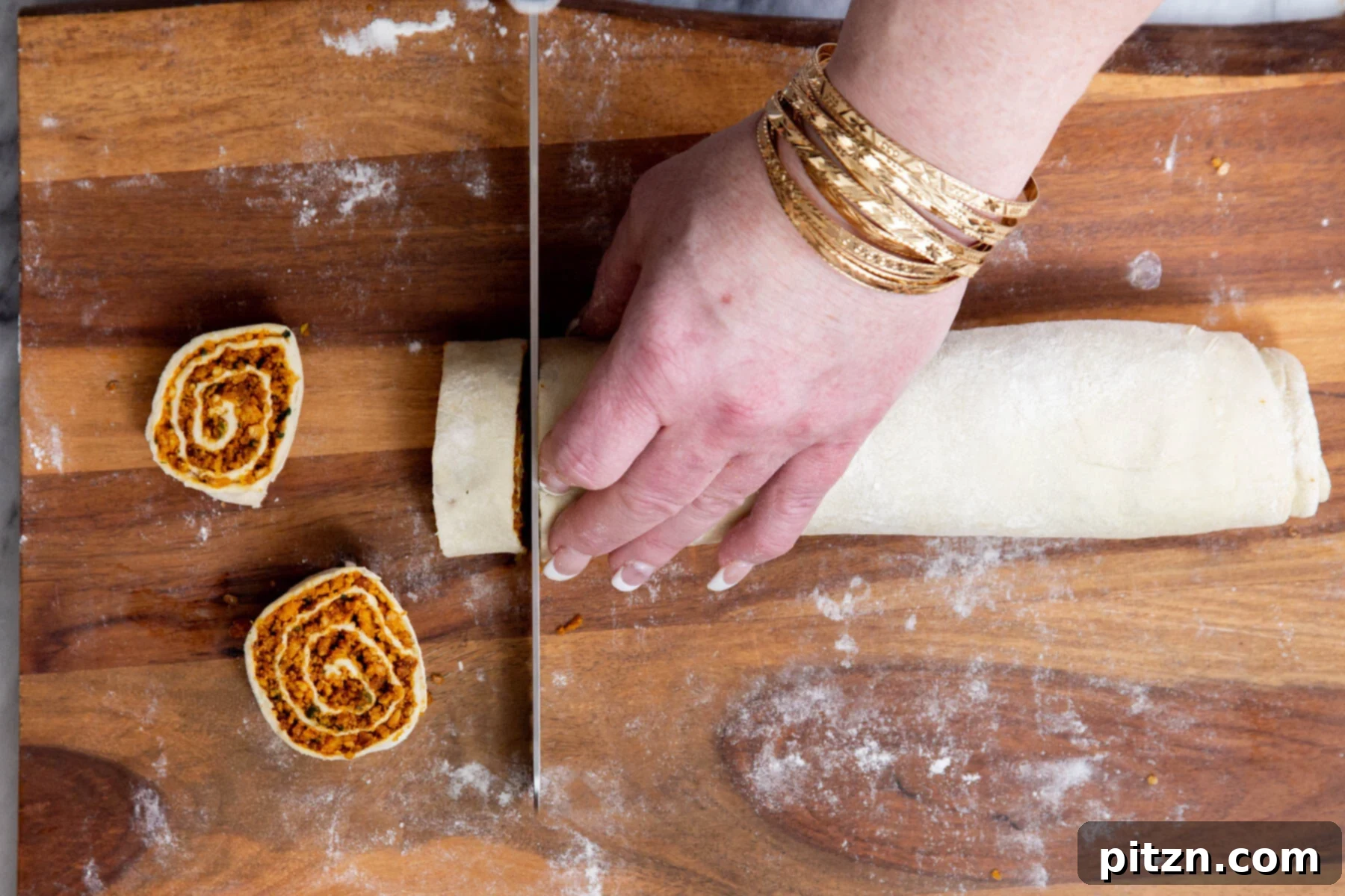 Vegan pinwheels being expertly cut into uniform slices on a chopping board using a sharp serrated knife.