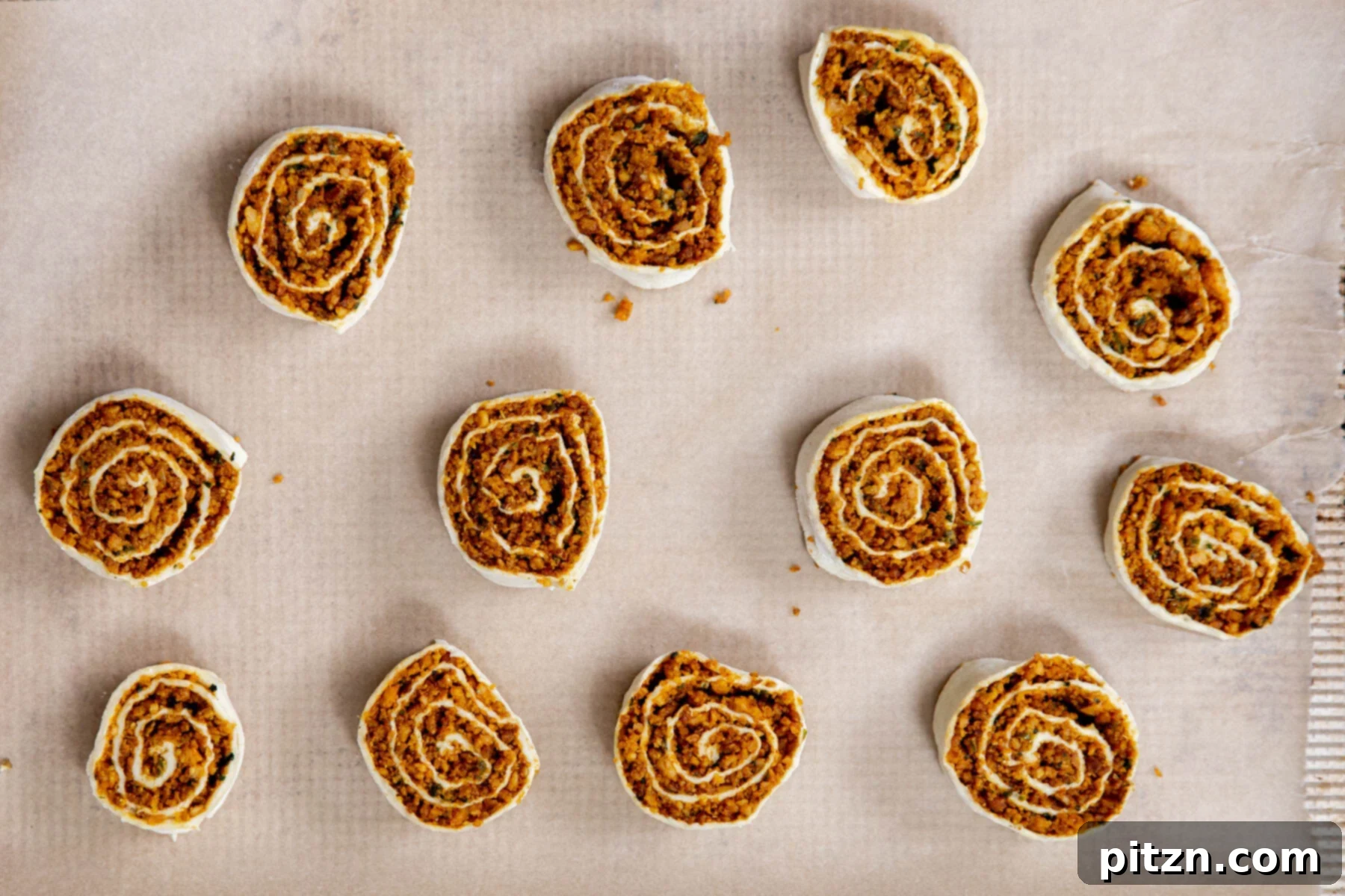 Unbaked vegan pinwheels carefully placed on a sheet of parchment paper, ready for the oven.