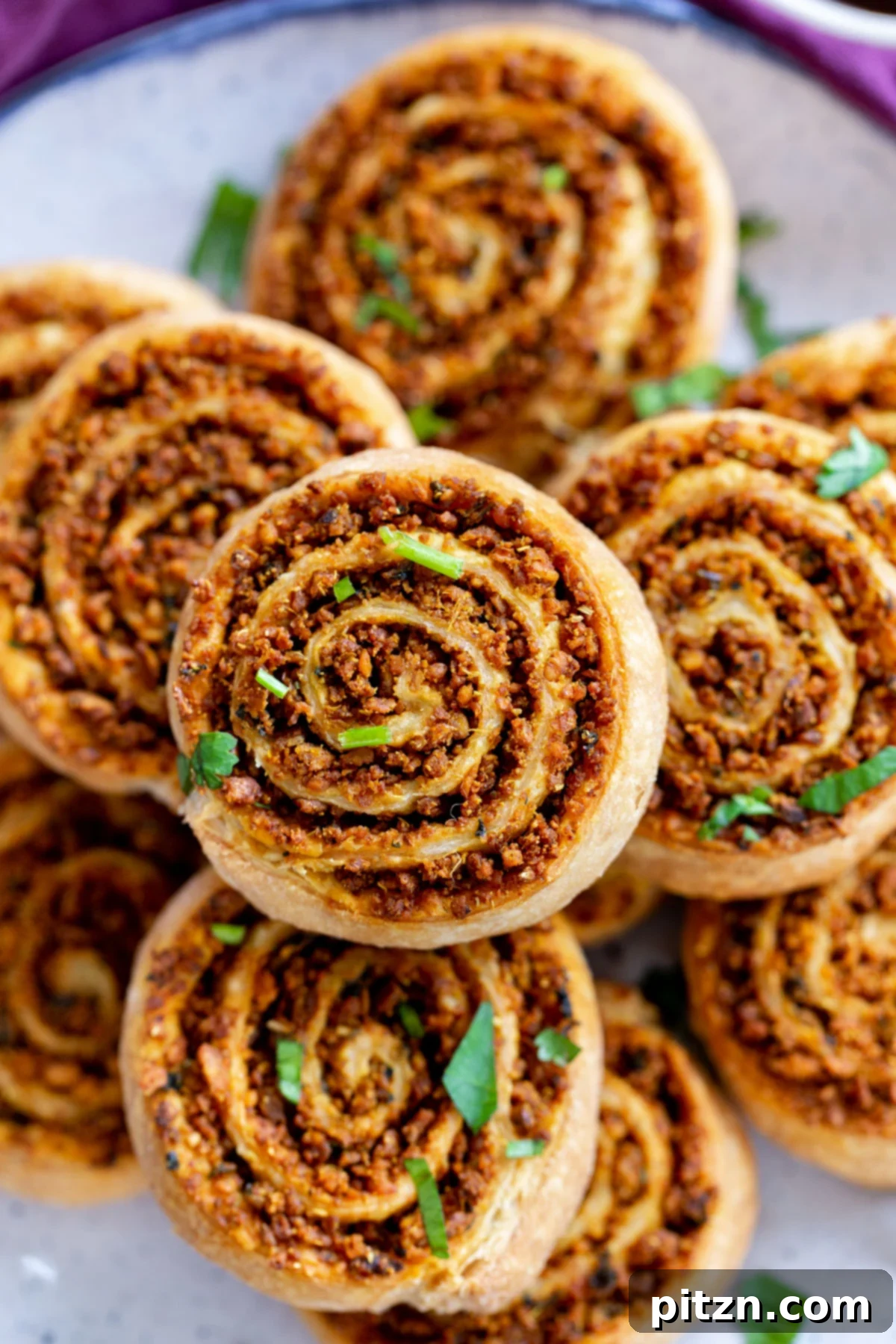 A close-up of beautifully baked puff pastry pinwheels with a golden crust and a visible, richly spiced moong dal lentil filling, ready to be served.