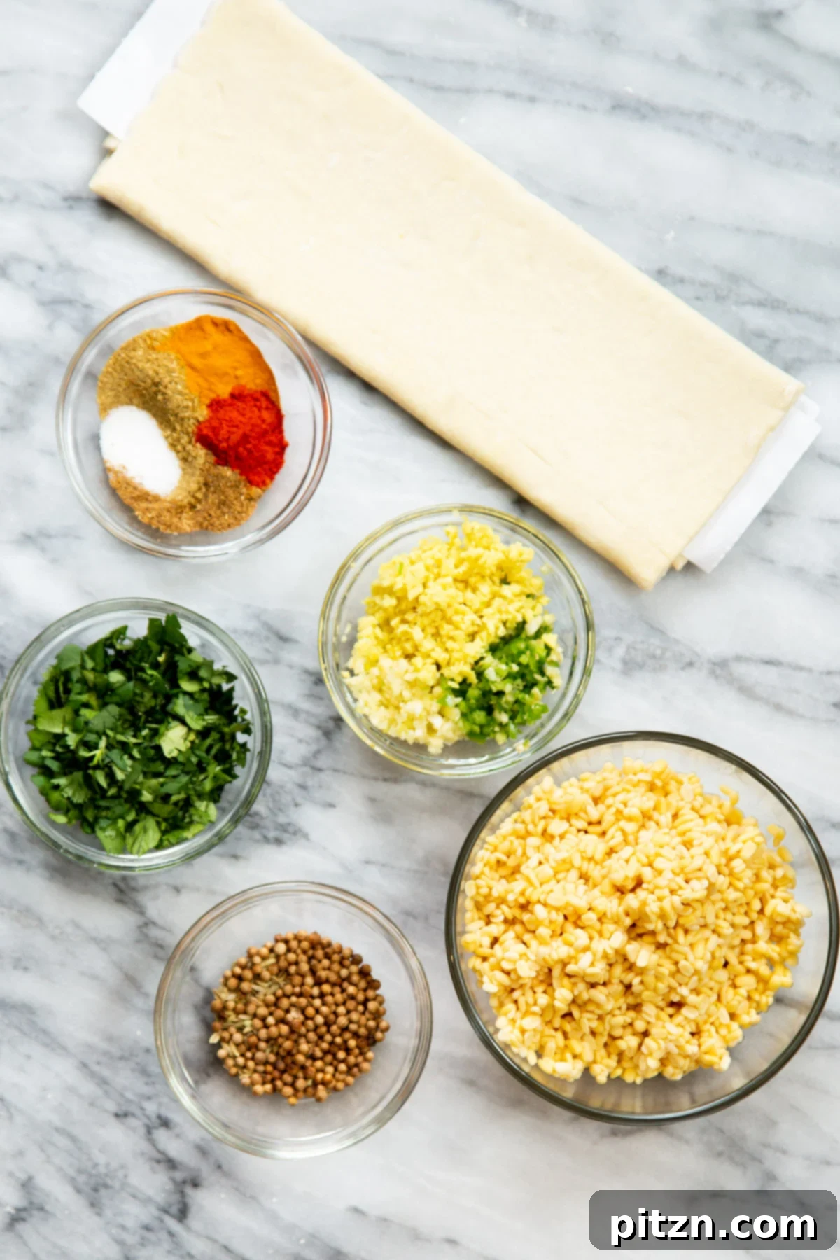 Various ingredients laid out for making Kachori Pinwheels, including soaked lentils, spices, herbs, and puff pastry.