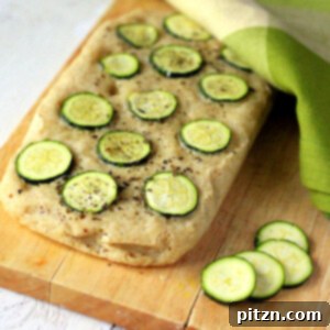 A loaf of Gluten-free Zucchini Basil Focaccia on a cutting board with slices of zucchini next to it