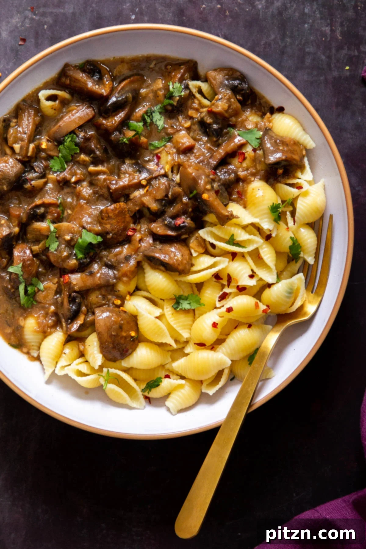 A white bowl filled with vegan Instant Pot garlic mushrooms served alongside shell pasta, illustrating a perfect meal pairing