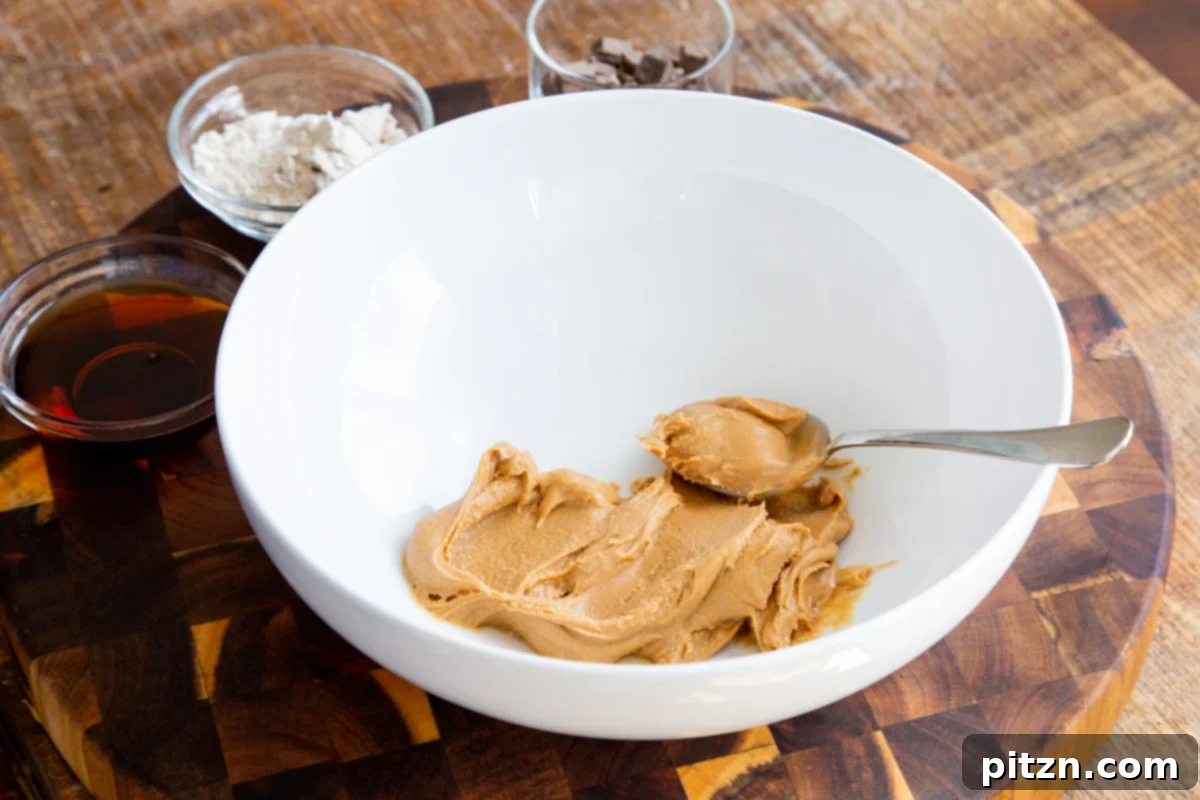 A white bowl filled with creamy, smooth peanut butter and a spoon, ready for mixing.