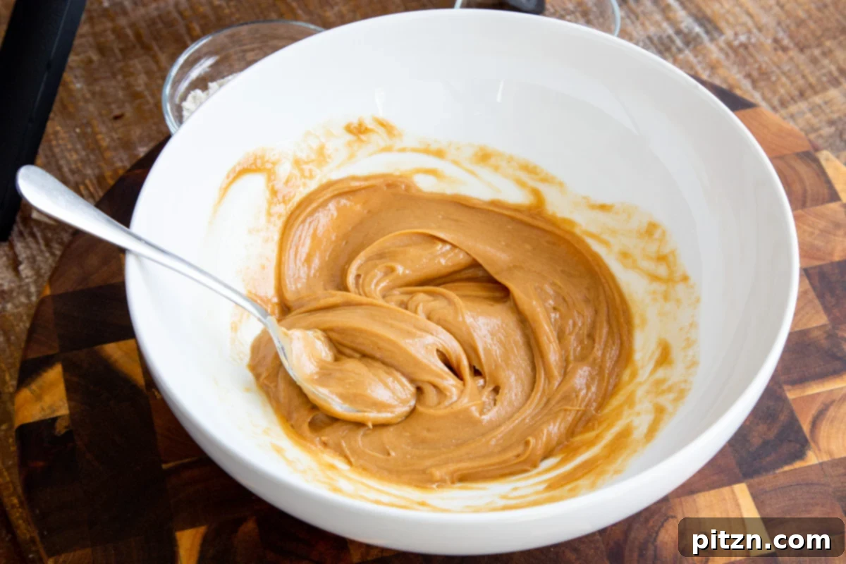 Warmed, smooth peanut butter being stirred with a spoon in a white bowl, showing its creamy texture.