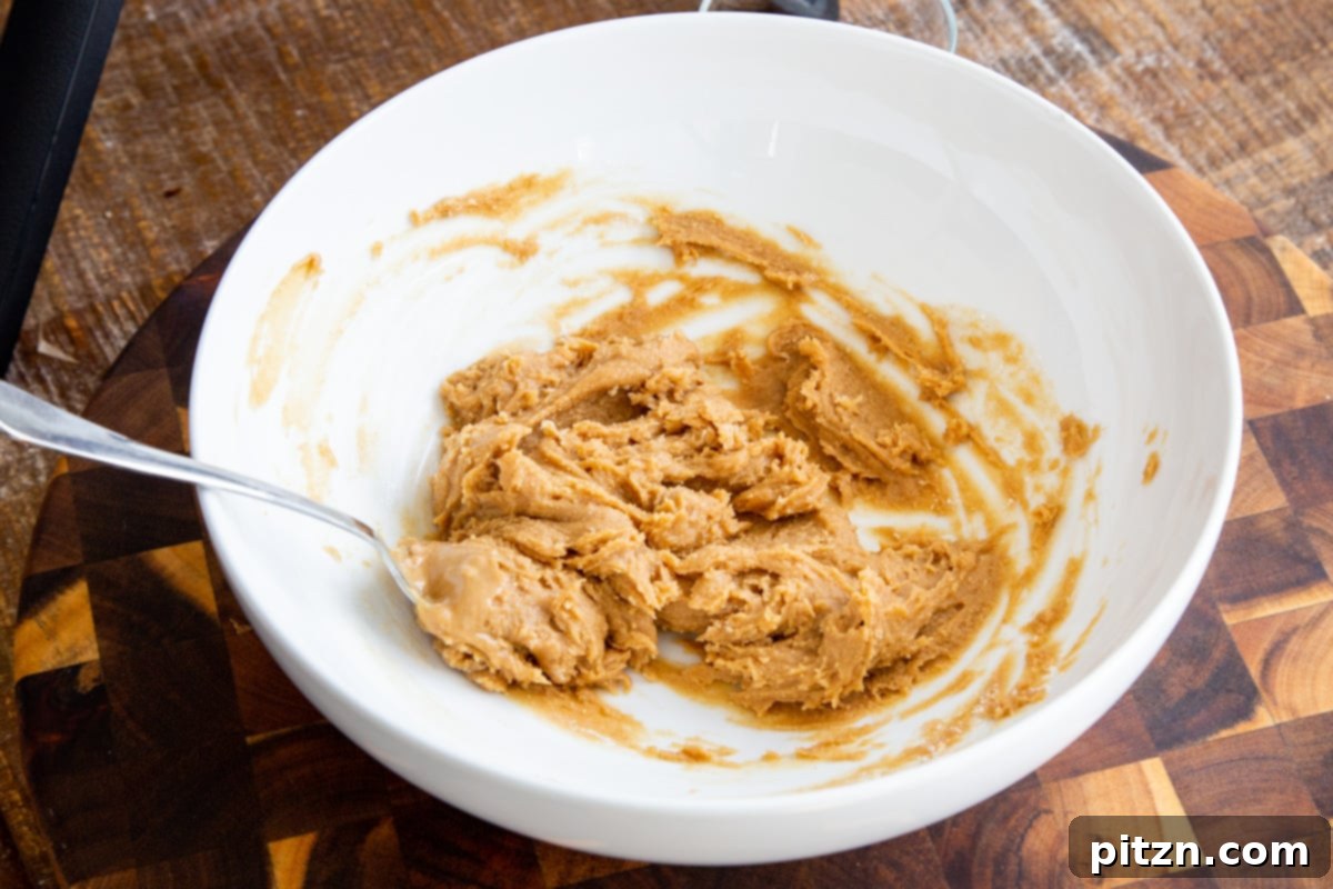 Peanut butter and almond flour being expertly stirred together in a clean white bowl, demonstrating the mixing process for the cookie dough.