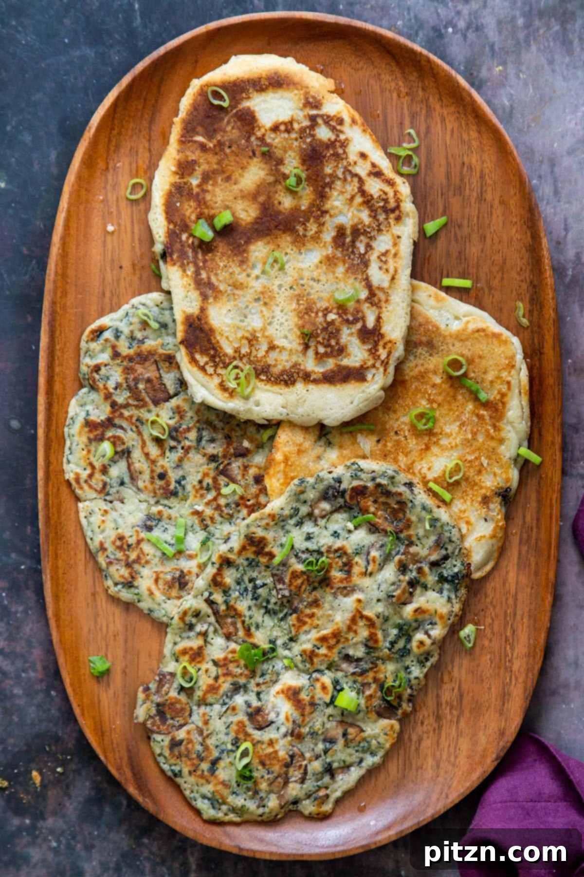 Spinach and Mushroom Stuffed Almond Flour Naan 2 A wooden plate with 4 spinach mushroom naan breads, garnished with fresh green onions