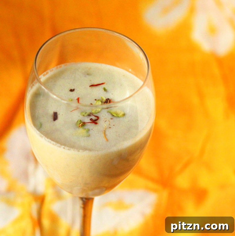 A close-up of a glass of Vegan Thandai, showing its creamy texture and rich color, with scattered nuts nearby.