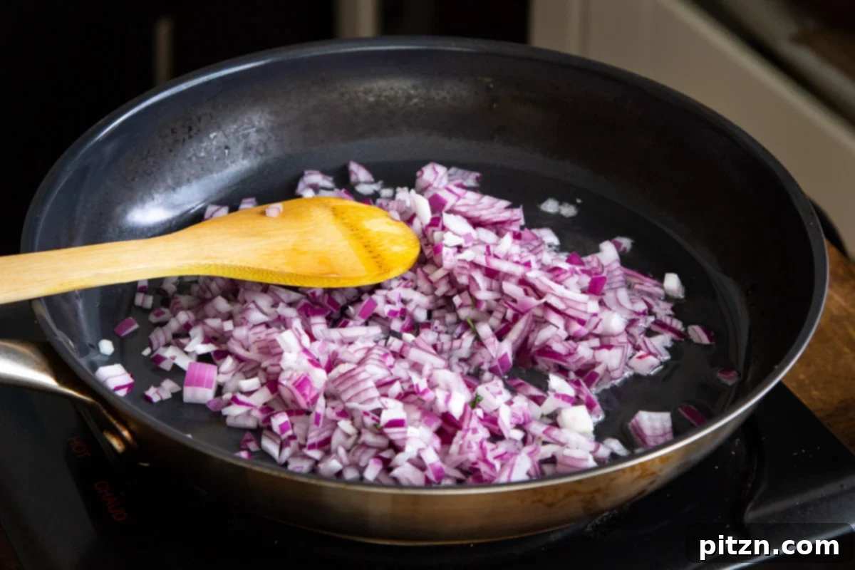 Plant-Based Chicken Changezi 10 Finely diced red onions sautéing in a black skillet, turning golden brown for the curry base.
