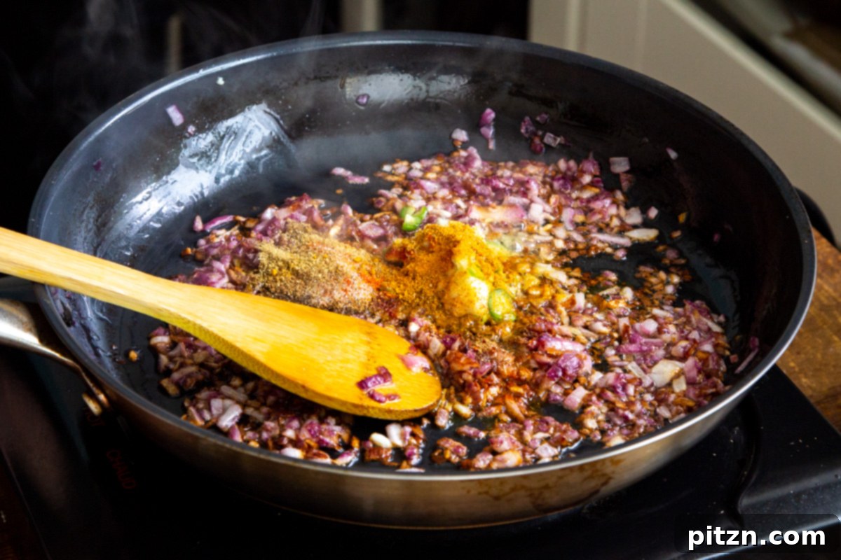 Plant-Based Chicken Changezi 12 Assorted Indian spices being added to the sautéed onions, ginger-garlic paste, and chili in a frying pan.