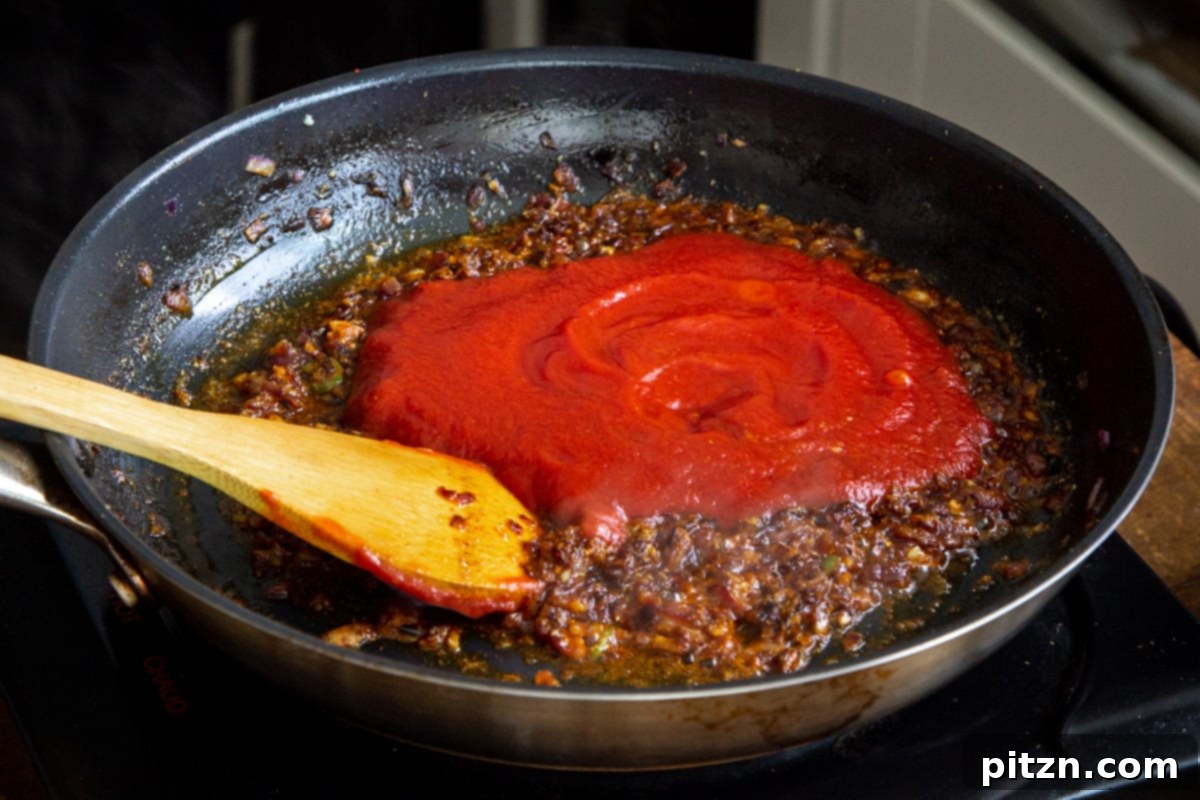 Plant-Based Chicken Changezi 13 Tomato puree being stirred into the fragrant spiced onion mixture in a frying pan.