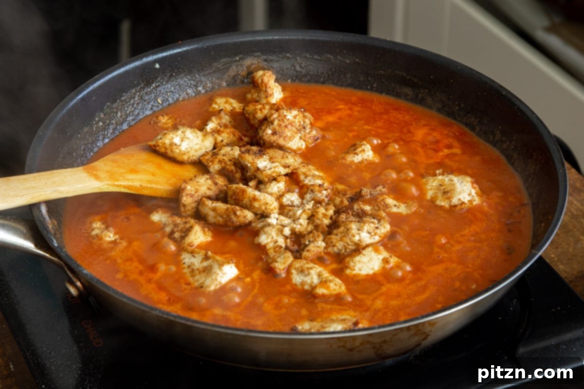 Plant-Based Chicken Changezi 16 Baked, marinated tofu chunks being added to the rich tomato-coconut gravy in a skillet.