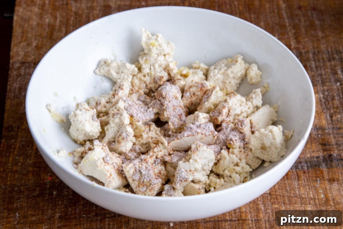 Plant-Based Chicken Changezi 7 Torn tofu pieces in a white bowl, coated with a blend of cornstarch and Indian spices, ready for baking.
