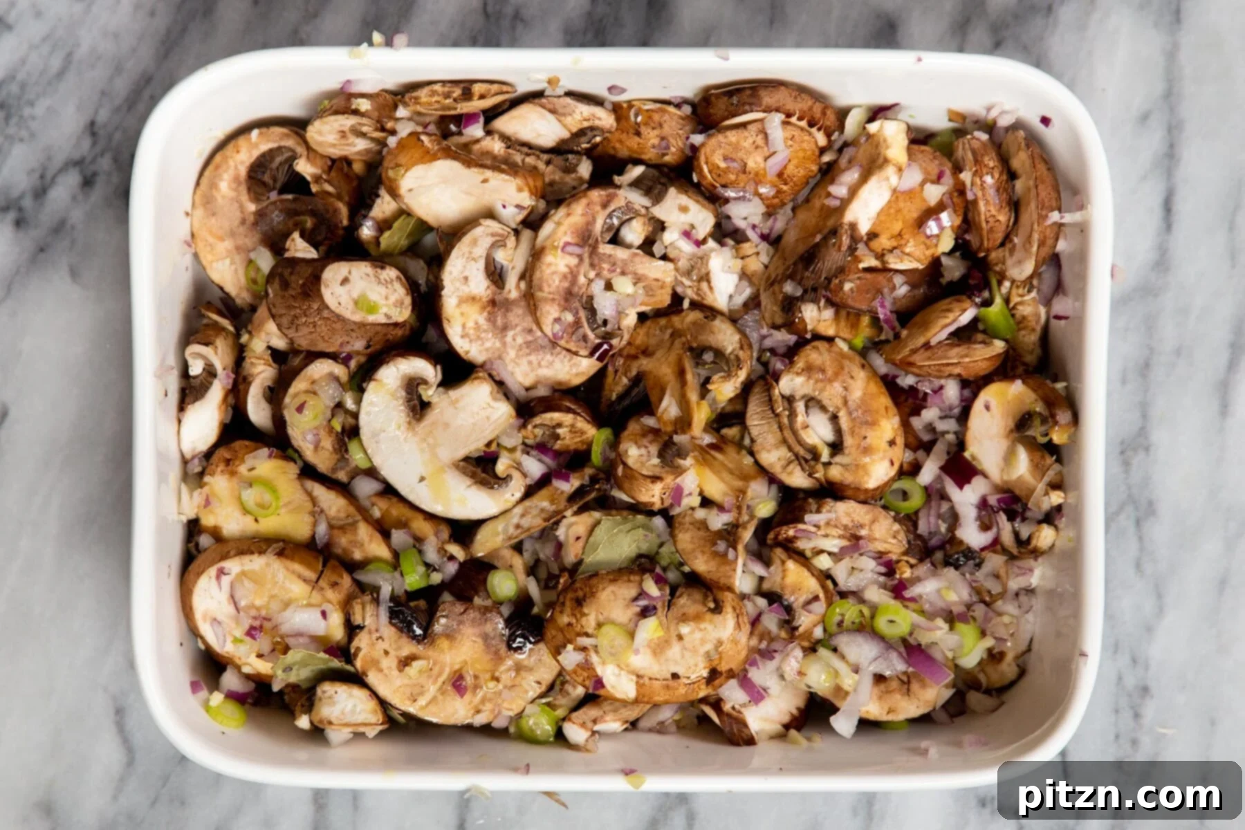 Sliced mushrooms, minced garlic, and chopped green onion arranged in a casserole dish, ready for roasting.