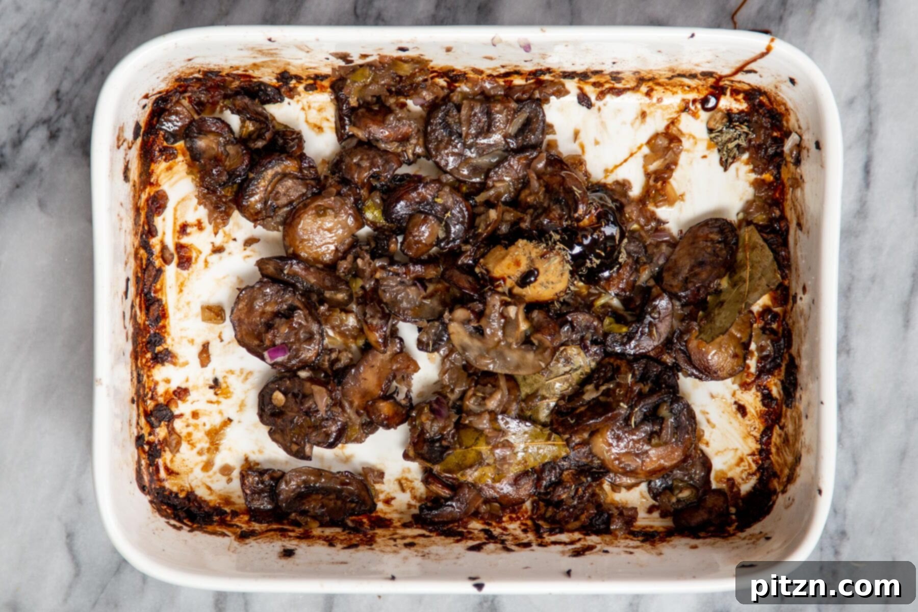 Deeply caramelized mushrooms in a white casserole dish, having achieved a rich golden-brown color from baking.